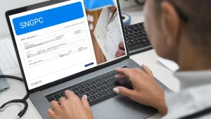 Mesa de planejamento com prancheta contendo o título Planejamento Tributário para Farmácias e gráfico de barras, ao lado de documentos financeiros, calculadora, óculos e frasco com comprimidos, em ambiente de farmácia.